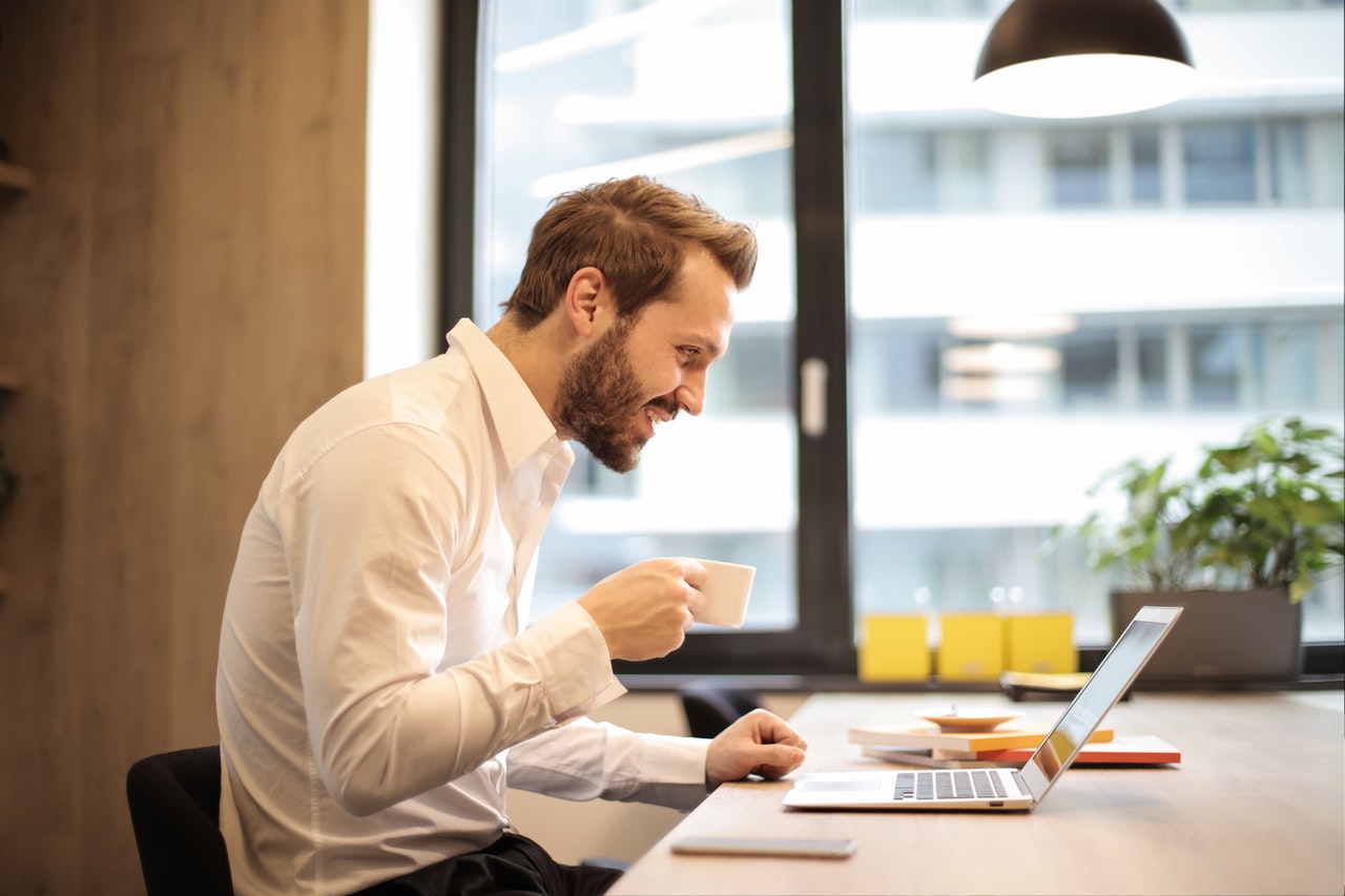 man-holding-teacup-infront-of-laptop-on-top-of-table-inside-925786