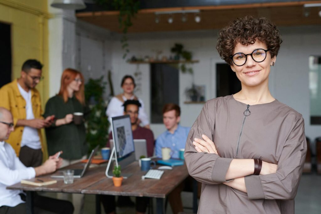 Une femme d'affaires souriante aux cheveux bouclés se tient avec confiance dans un espace de bureau moderne avec ses collègues.