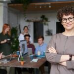 Une femme d'affaires souriante aux cheveux bouclés se tient avec confiance dans un espace de bureau moderne avec ses collègues.